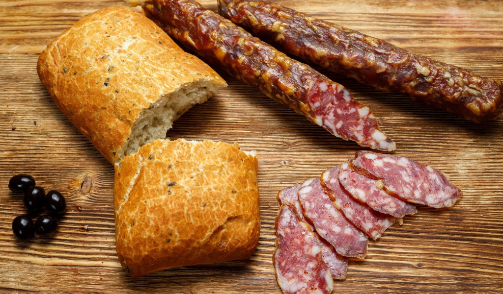 Сухая колбаса на столе с батоном и оливками