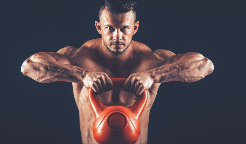 Накаченный парень поднимает тяжелую гирю на черном фоне