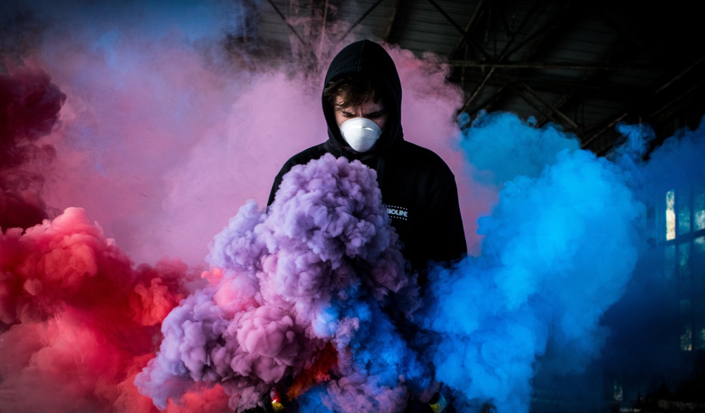 Мужчина в маске с разноцветными дымовыми шашками
