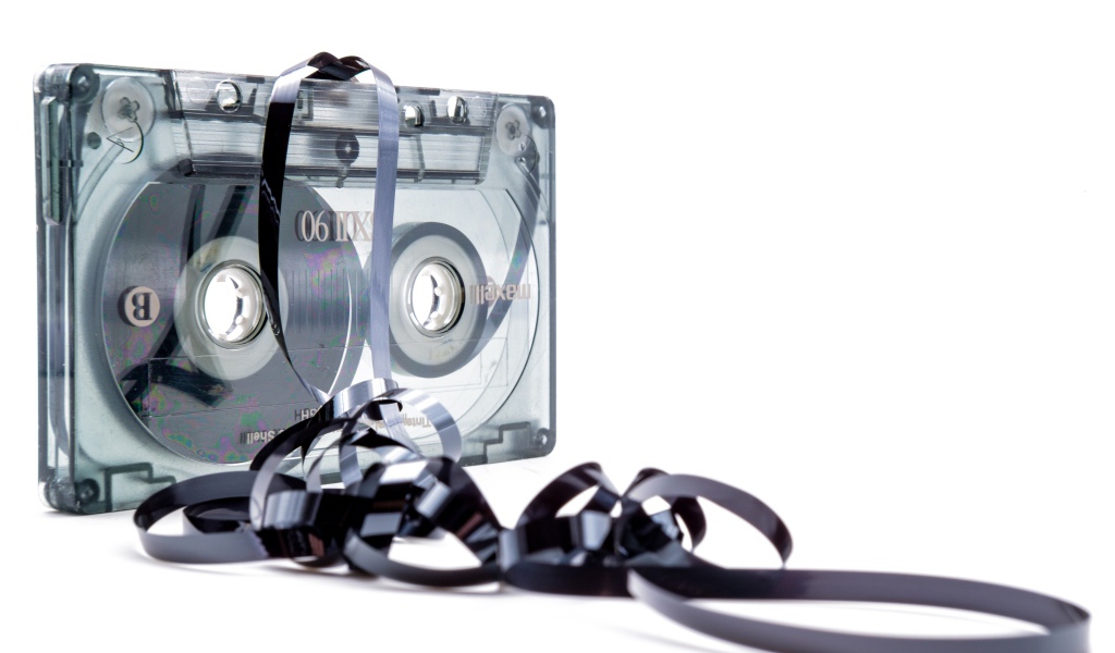 Магнитофонная кассета в размотанной пленкой на белом фоне