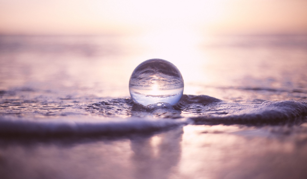 Прозрачный стеклянный шар лежит на пене в море