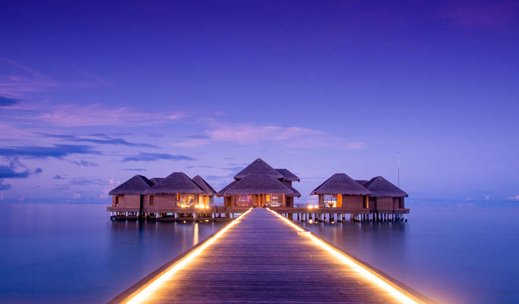 Мост с подсветкой идет к домам на сваях в океане