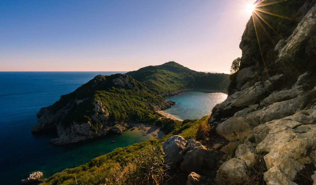 Яркое солнце за скалой у тихого моря