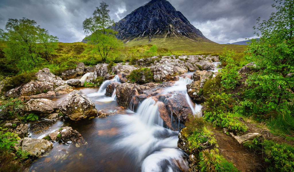 Быстрая вода в реке на фоне высокой горы под грозовым небом 