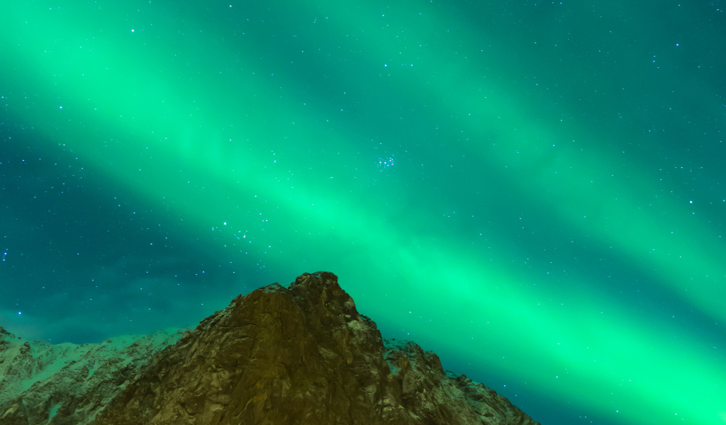Зеленое северное сияние над верхушкой скалы в небе 