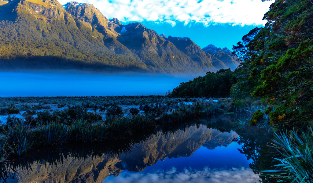 Горы и небо отражаются в голубой воде озера 
