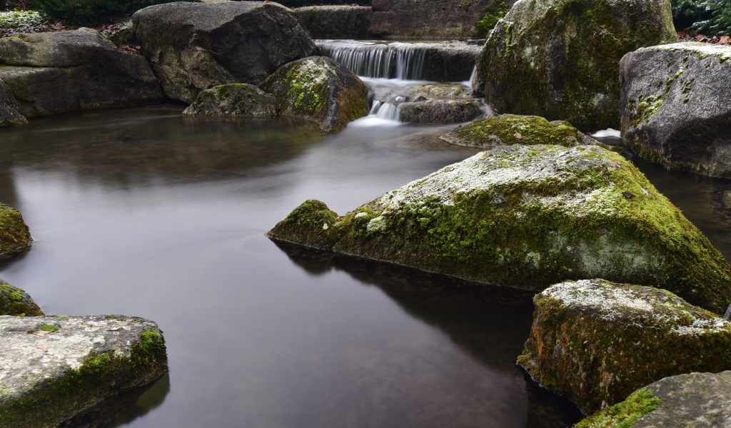 Вода стекает по камням в пруд с большими покрытыми мхом камнями