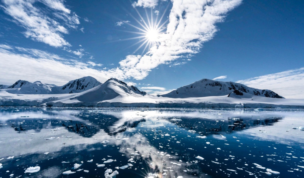 Белые облака в солнечном небе отражаются в озере у заснеженных гор 