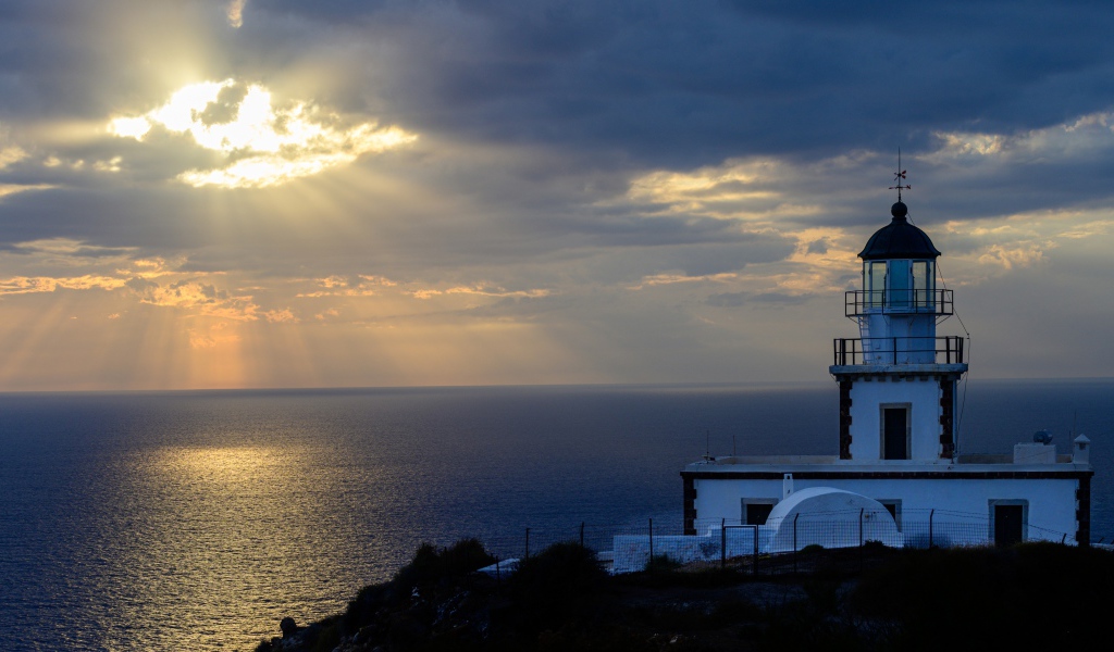 Белый маяк на берегу в лучах солнца у моря 