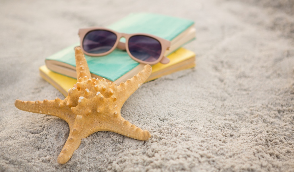 Книги, очки и морская звезда на белом песке 
