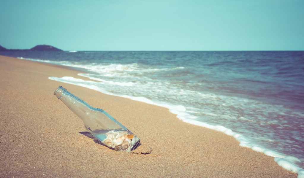 Бутылка с ракушками на песке у моря
