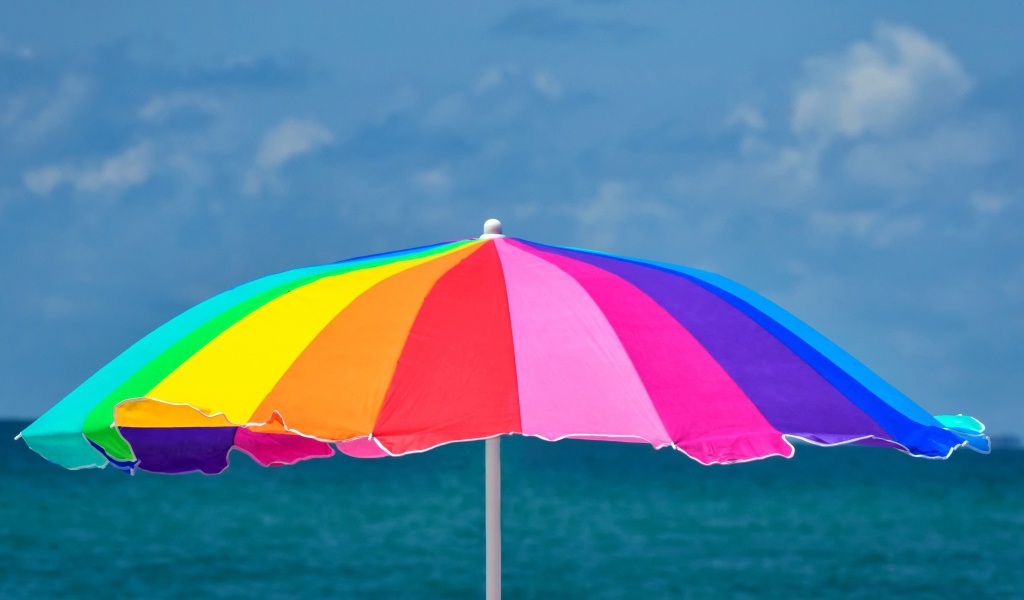 Большой разноцветный пляжный зонт на фоне моря