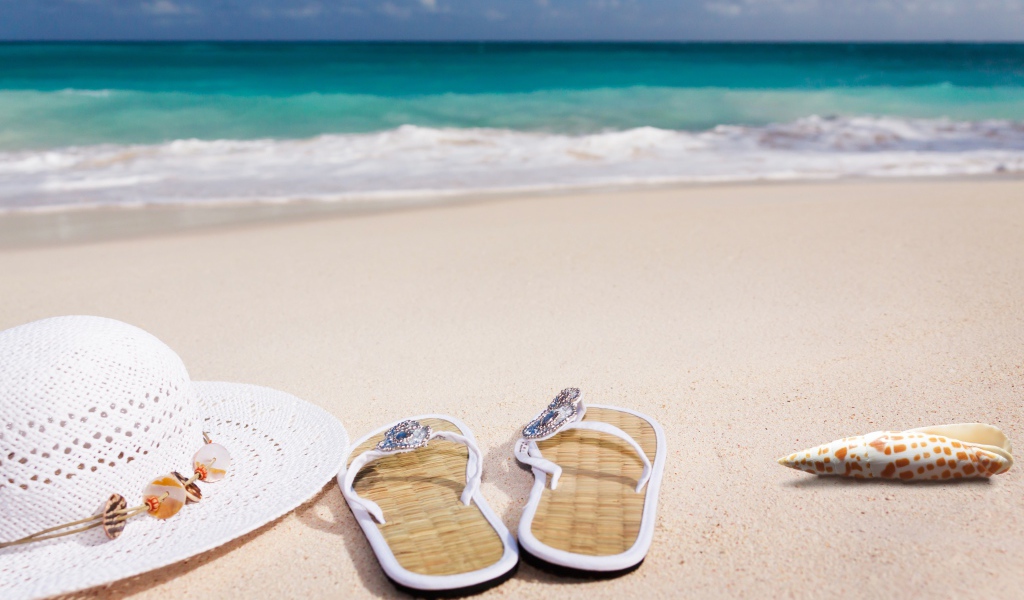 Сланцы, шляпа и ракушка на песке у моря 