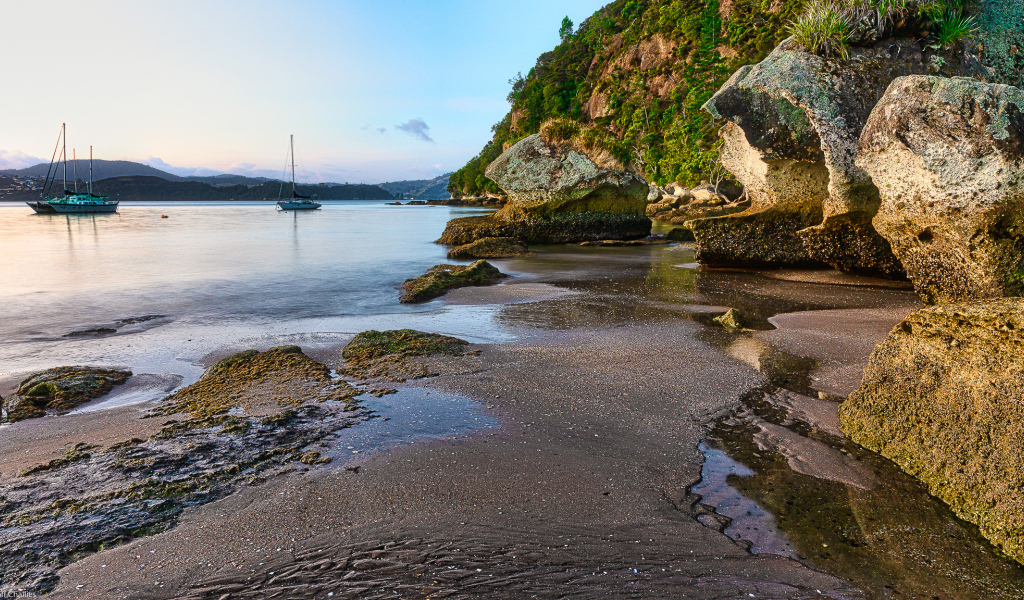 Мокрый песок и большие каменные глыбы на берегу залива