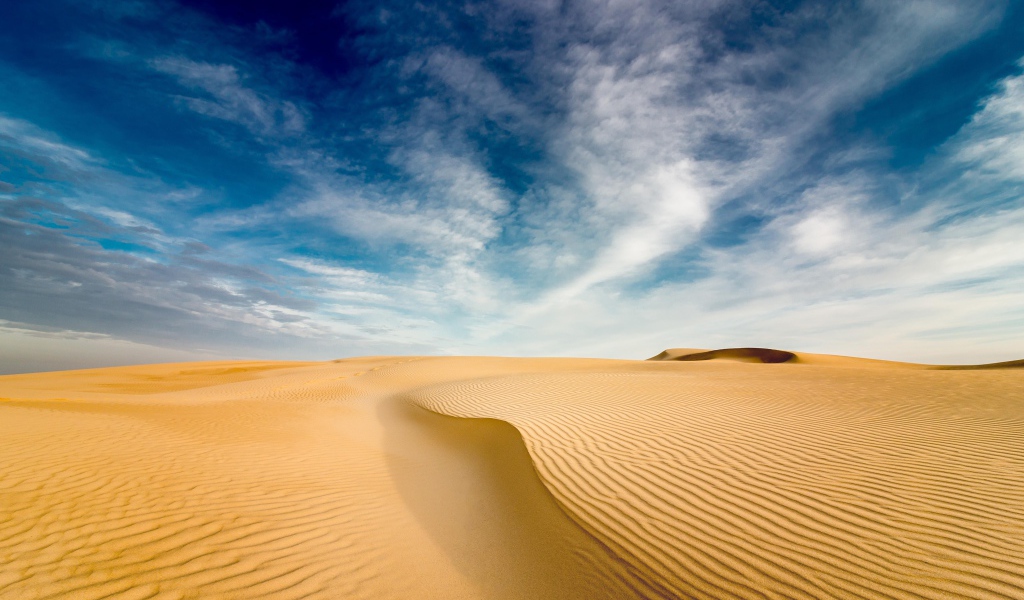 Песчаная дюна под голубым небом с белыми облаками 