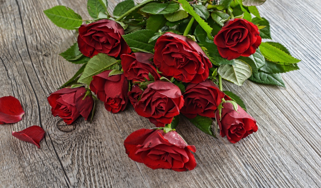 Красивый букет алых роз с зелеными листьями на деревянном столе