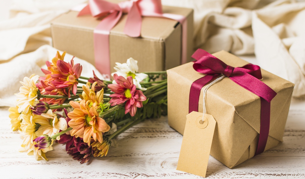 Букет разноцветных хризантем с подарками на столе 