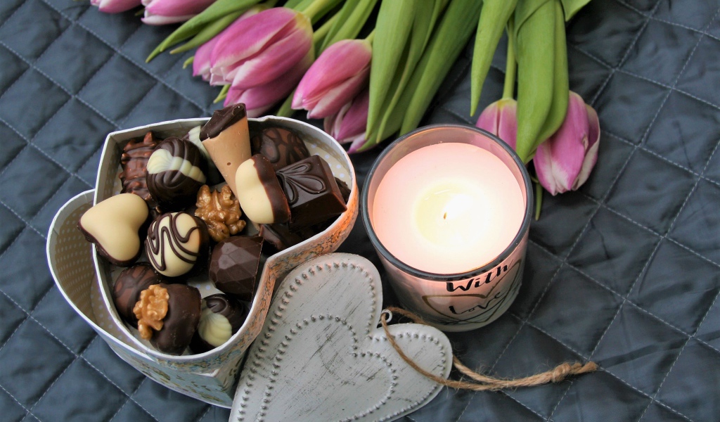 Букет розовых тюльпанов на кровати со свечой и коробкой конфет