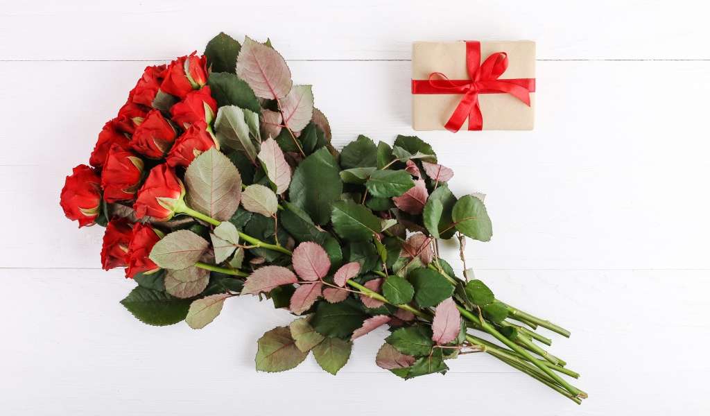 Bouquet of prickly red roses with a gift on a white background