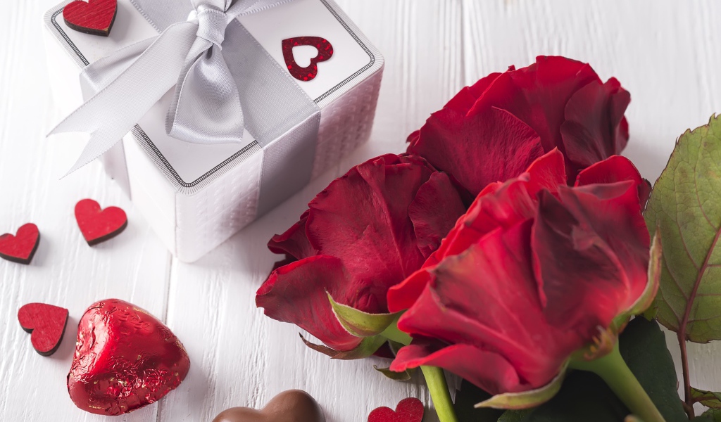 Букет красных роз на столе с конфетами и подарком