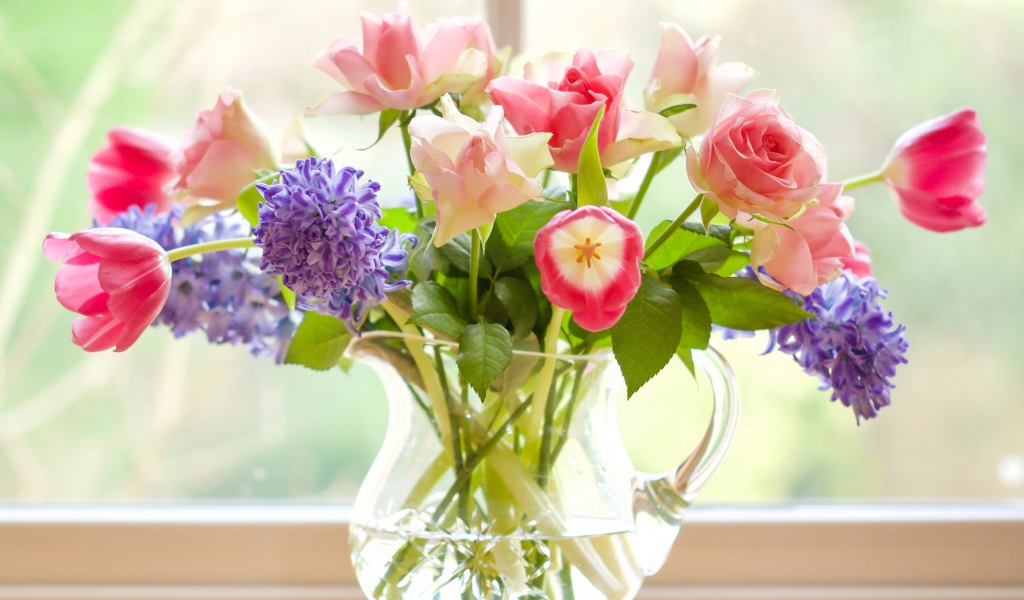 Букет роз, тюльпанов и гиацинтов в стеклянной вазе у окна