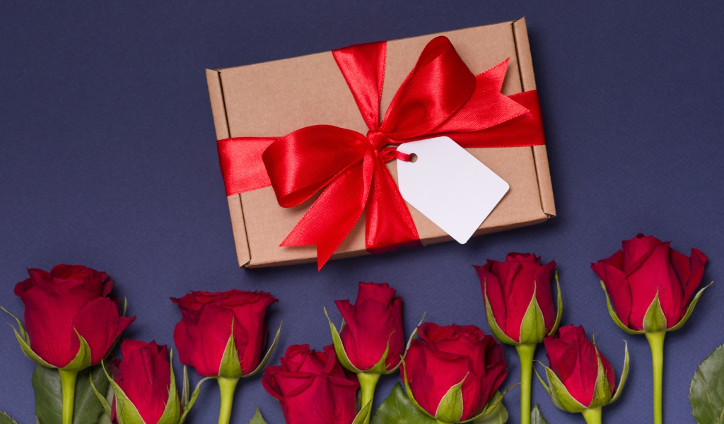 Подарок с красным бантом на столе с розами