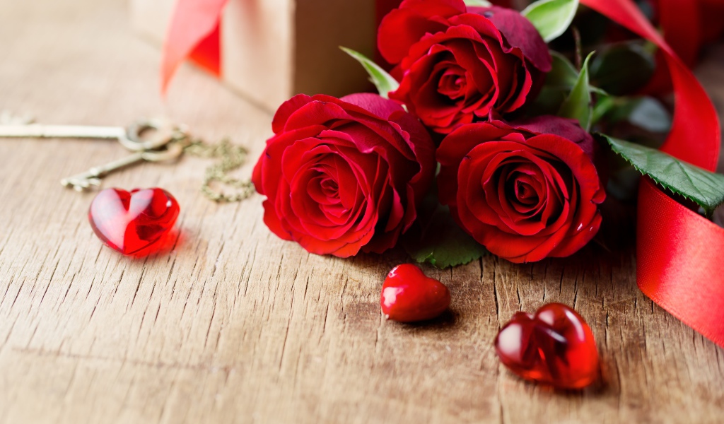 Три красивые красные розы на столе с сердечками и ключами