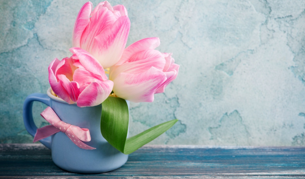 Три розовых тюльпана в чашке на столе 
