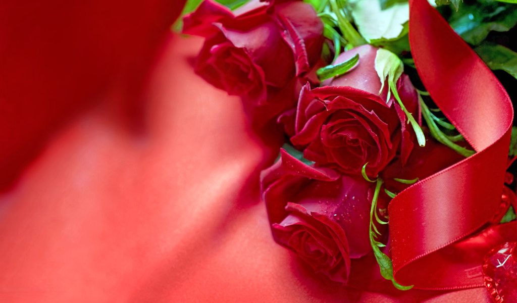 Три красные розы с атласной лентой на красной ткани