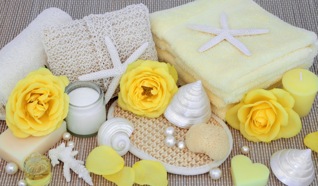 Желтые розы на столе с полотенцем, ракушками и мылом