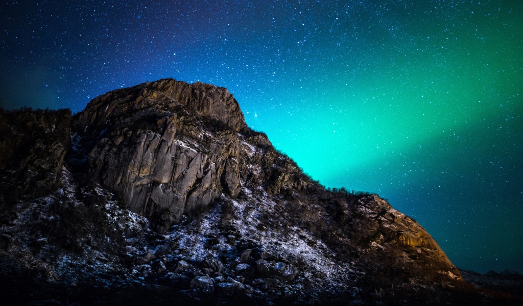 Красивое зеленое полярное сияние в звездном небе над горой 