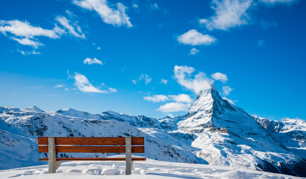Лавка в заснеженных горах под голубым ясным небом