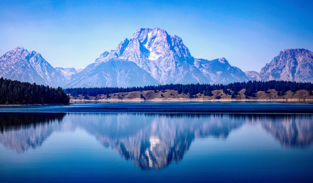 Высокие горы отражаются в озере под голубым небом