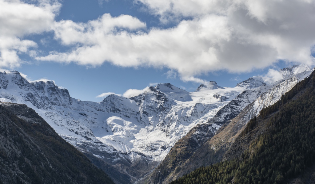 Заснеженные горы под голубым небом с белыми облаками