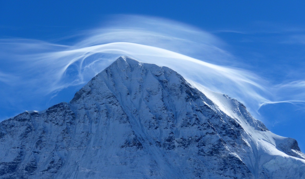 Белое облако в голубом небе над заснеженной горной вершиной