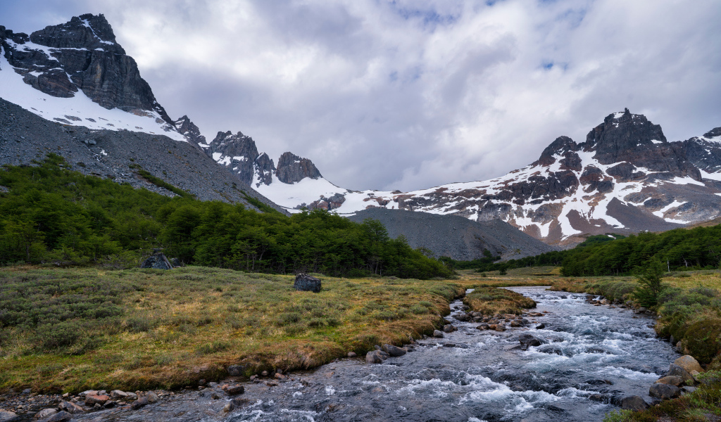 Быстрая река у заснеженных гор под густыми белыми облаками