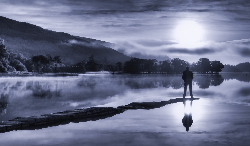 Мужчина стоит на мосту у озера ночью при свете луны