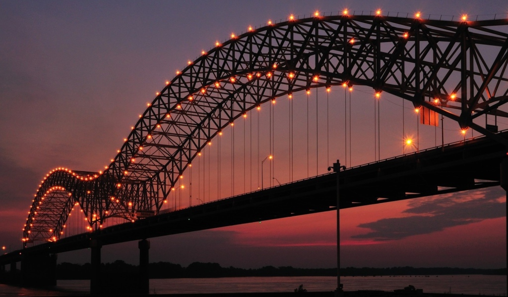 Арки на железном мосту с фонарями ночью через реку 