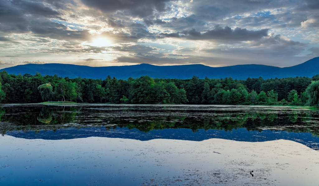 Солнце пробивается сквозь облака в небе над озером