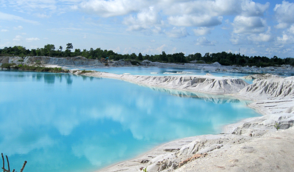 Белый песок на берегу водоема с голубой водой 
