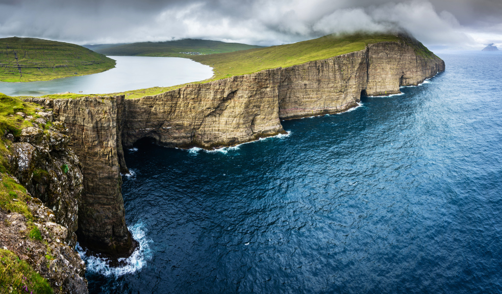 Ocean washed by a green cliff under a cloudy sky