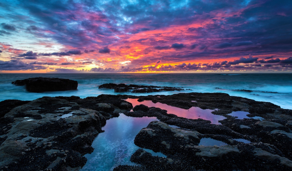 Восход яркого солнца над камнями в море