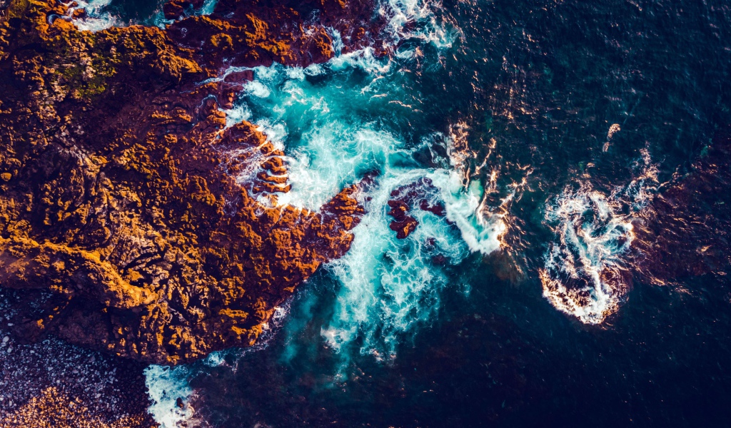 Белые морские волны бьются об камни, вид сверху