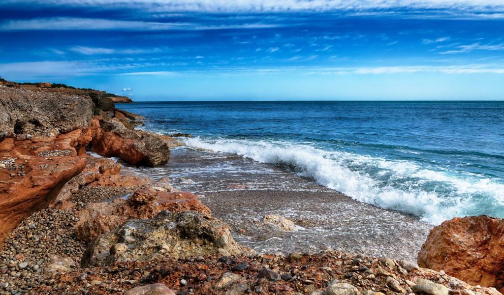 Белые волны на берегу моря с большими камнями под голубым небом