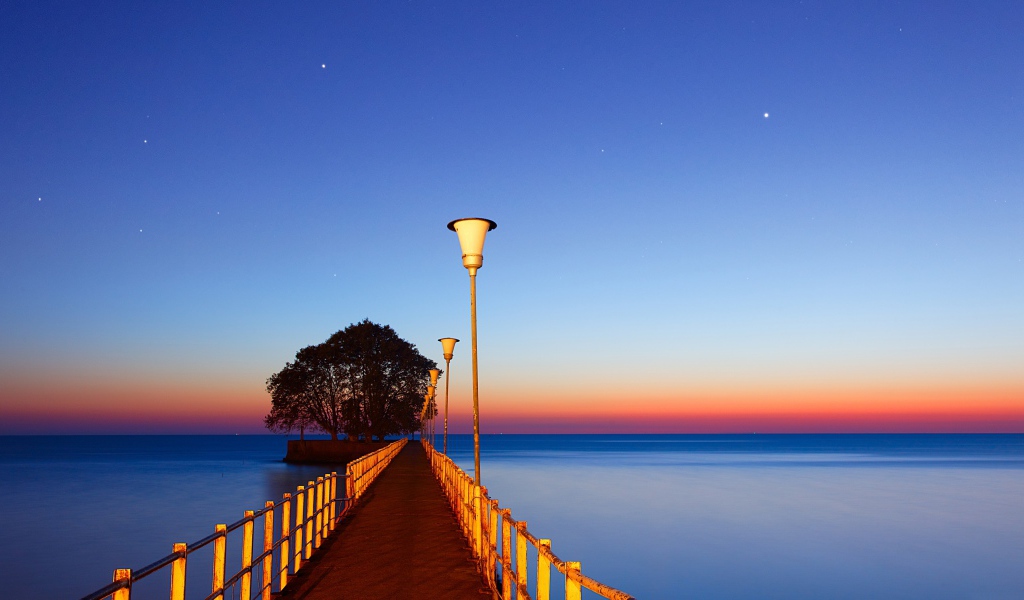 Мост в фонарями в море на закате 