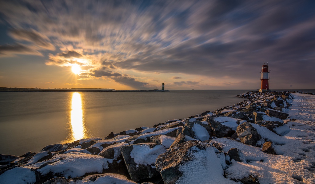 Заснеженные камни на берегу моря с маяком на закате