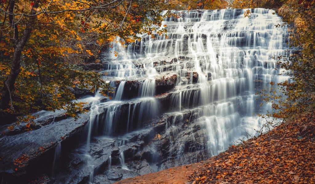 Быстрая вода водопада стекает по каскадам камней осенью