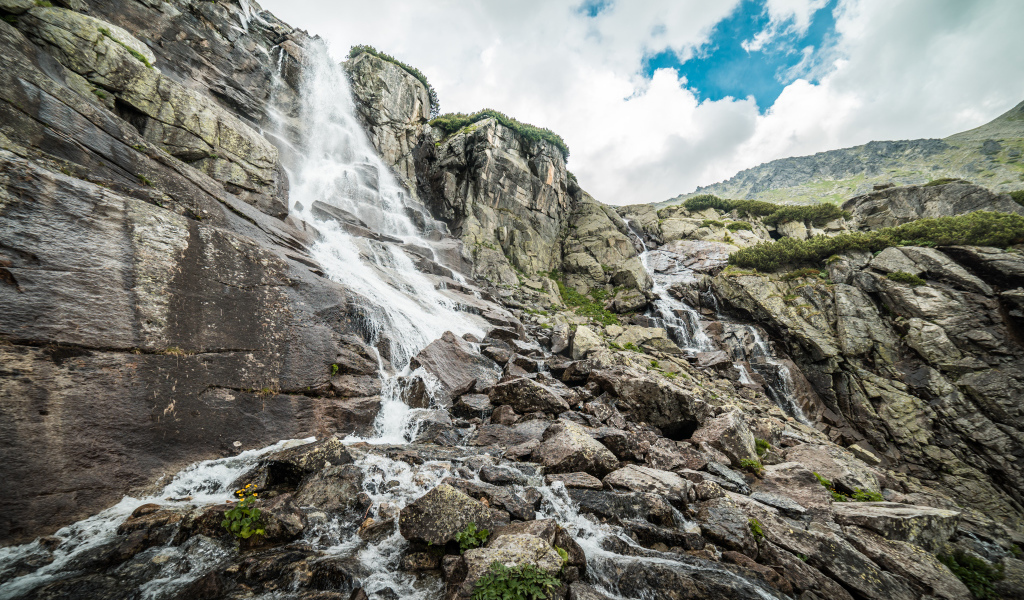 Водопад стекает по камням на фоне неба с белыми облаками