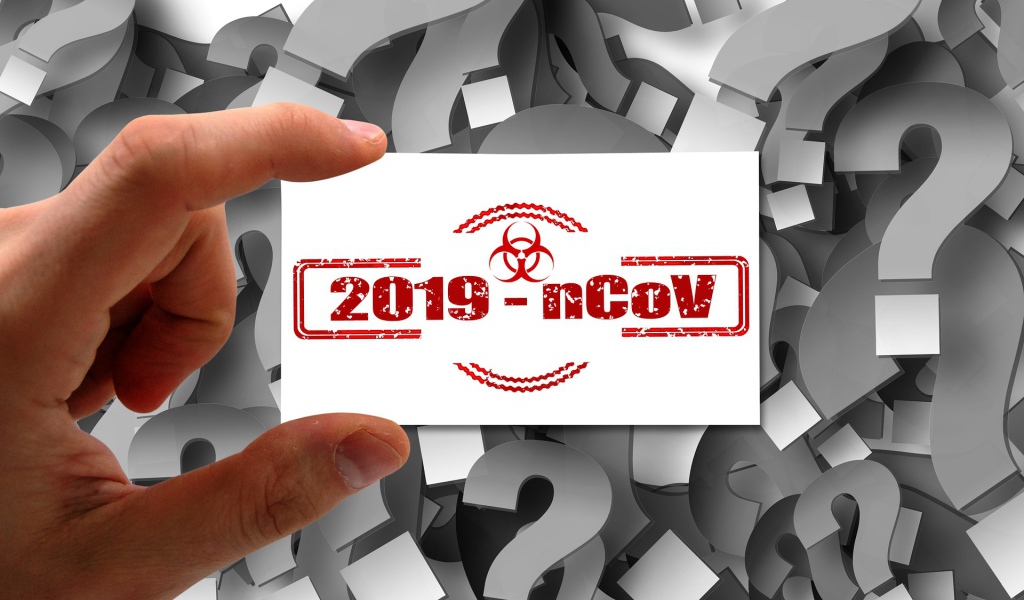 Табличка коронавирус covid-19 в руке на фоне знаков вопроса