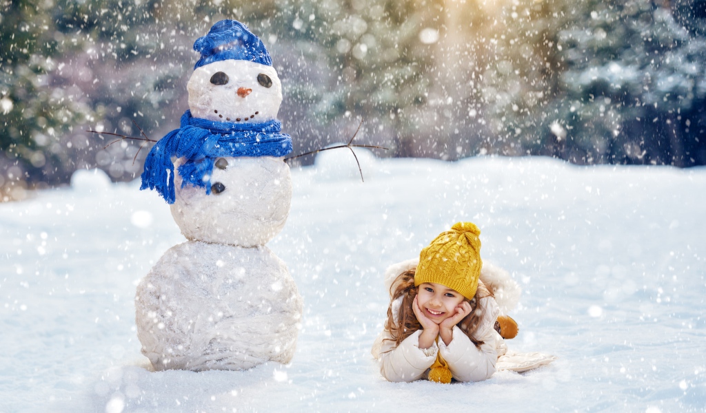 Милая девочка лежит на снегу у снеговика зимой